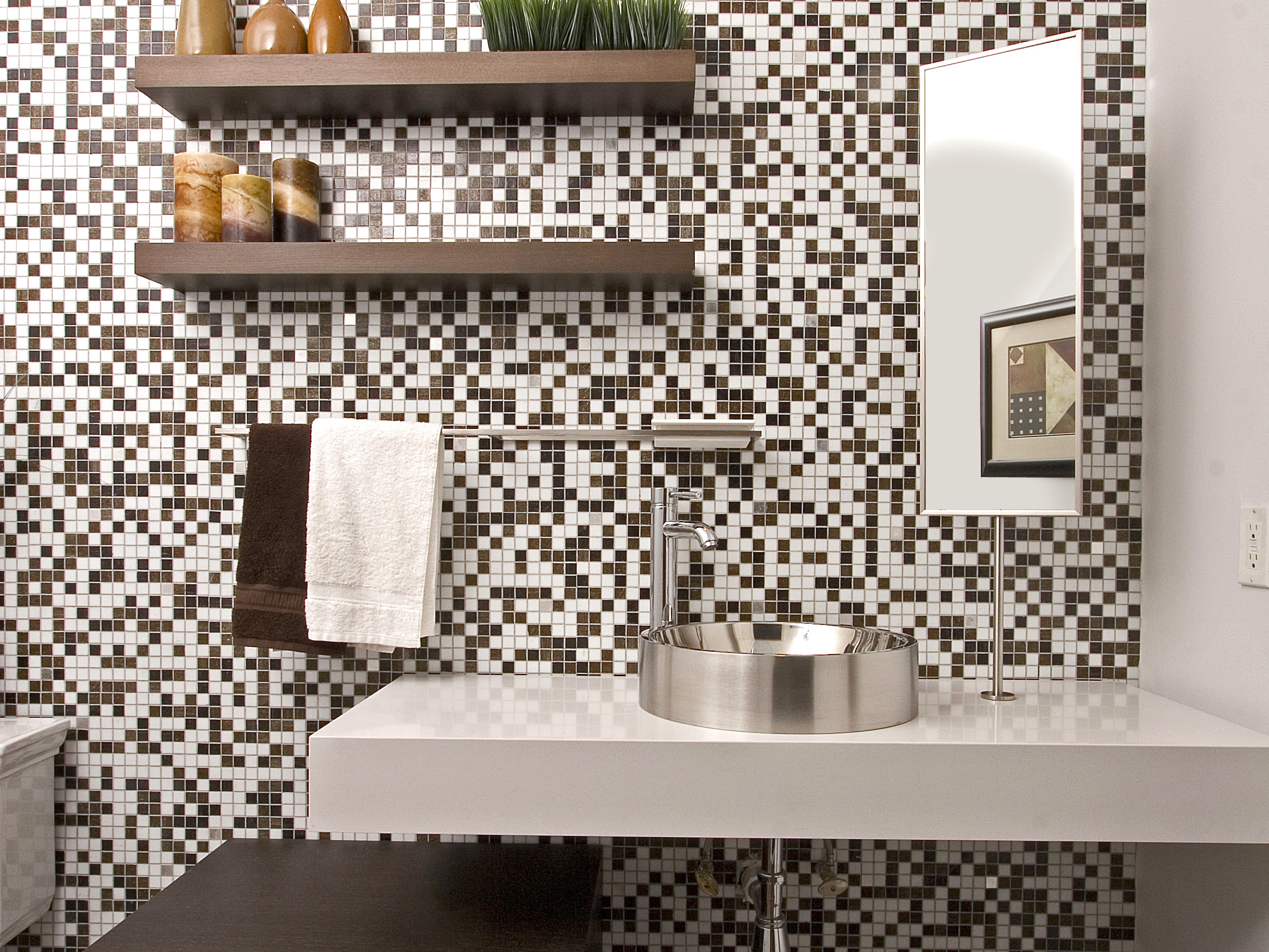 Brown bathroom, floating vanity with stainless steel sink and faucet, towel holder, mirror, floating shelf, and borwn and white tiled wall from ceiling to floor.